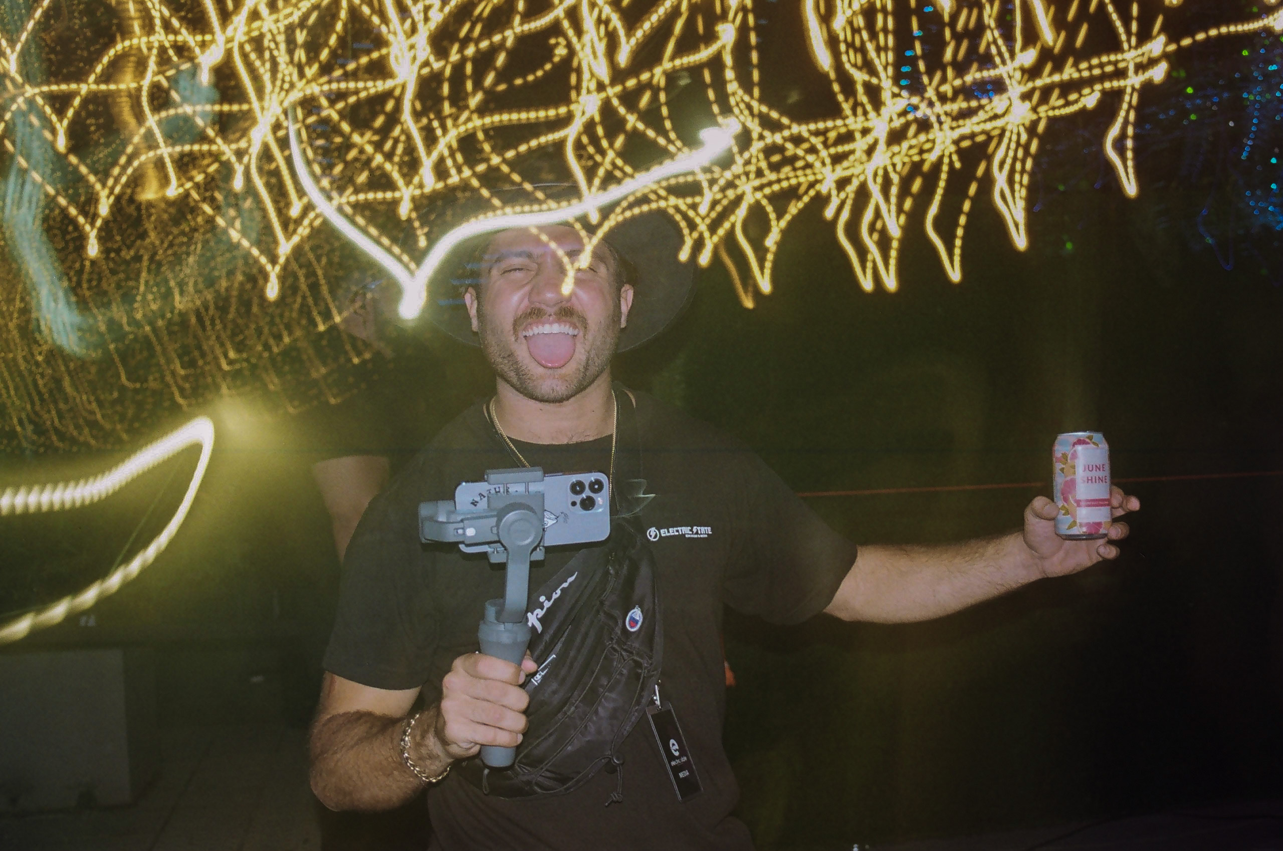 Event videographer poses for a picture; camera's exposure settings creates motion blur of surrounding lights around him.