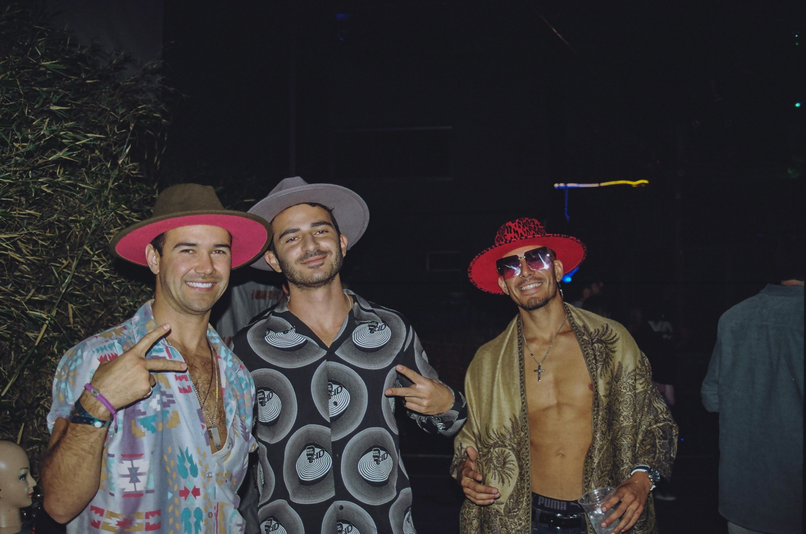 Three friends smile and stand for picture; two of them throw up peace signs.