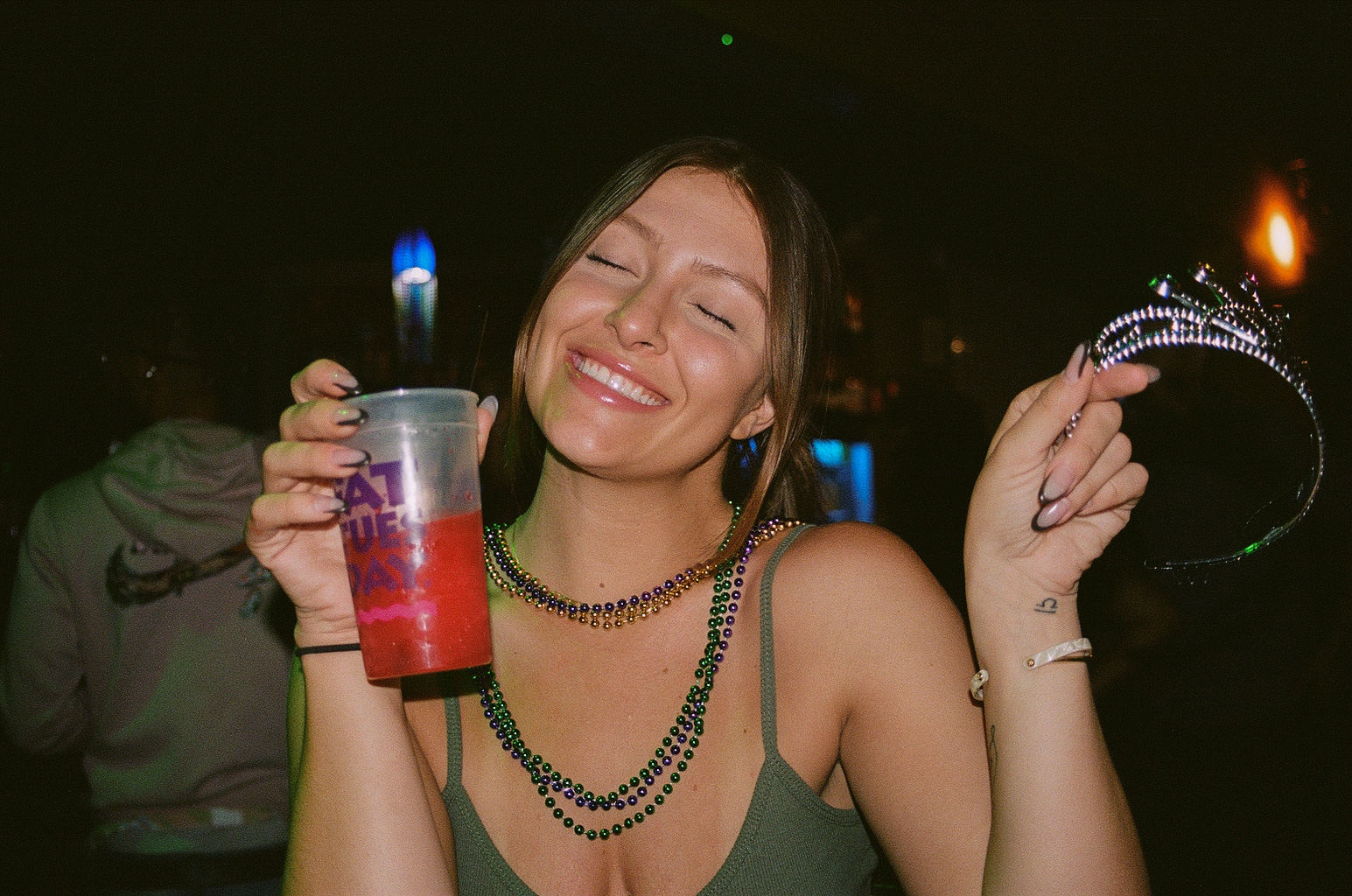 Friend smiles for a photo with her drink and plastic party tiara in hand during Mardi Gras celebrations at Fat Tuesday on Mill Avenue in Downtown Tempe.