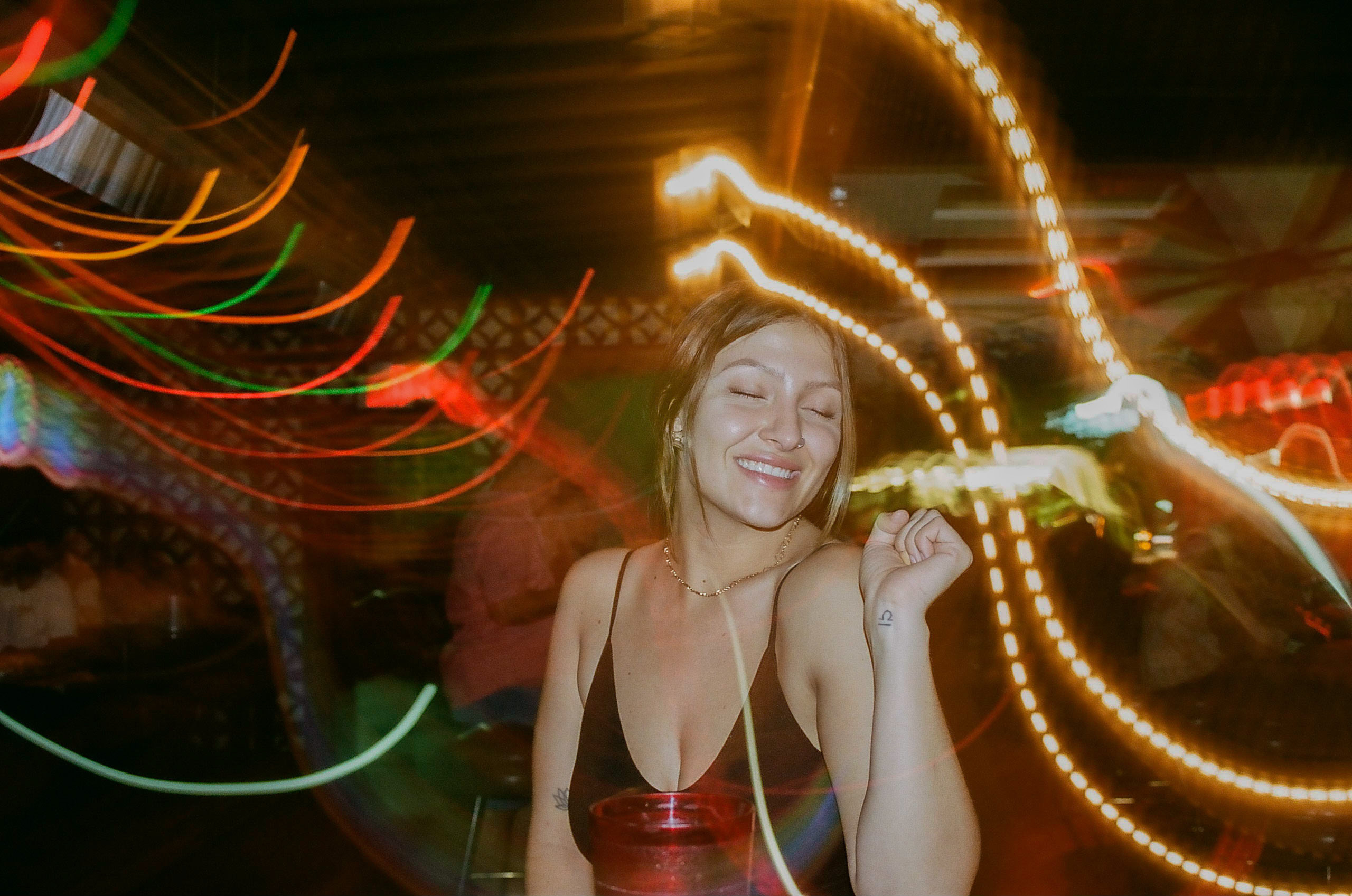 Friend poses for a picture during dinner at Shady Park in Tempe; camera's exposure settings creates motion blur of surrounding lights around her.