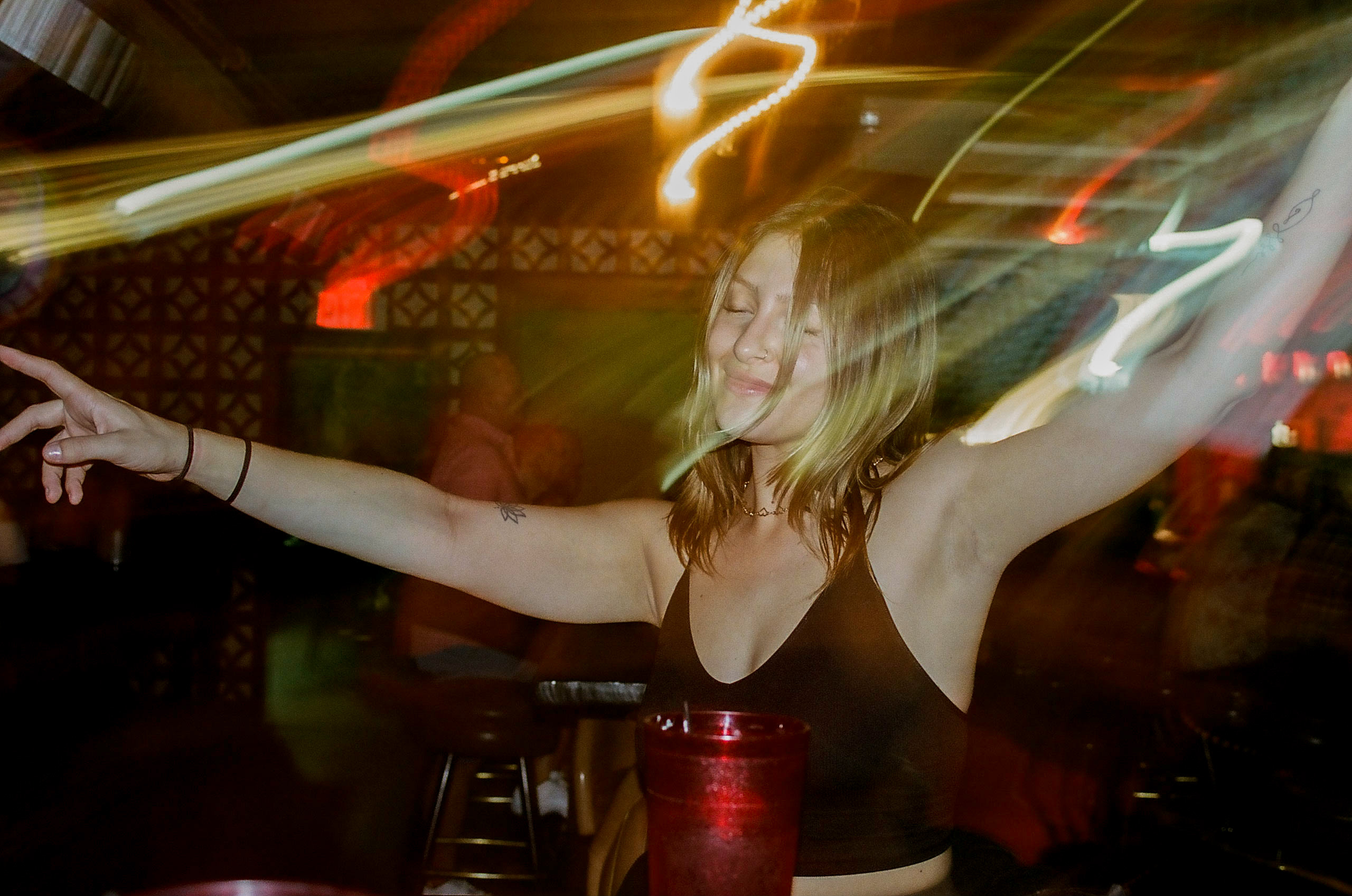 Friend poses for a picture during dinner at Shady Park in Tempe; camera's exposure settings creates motion blur of surrounding lights around her.