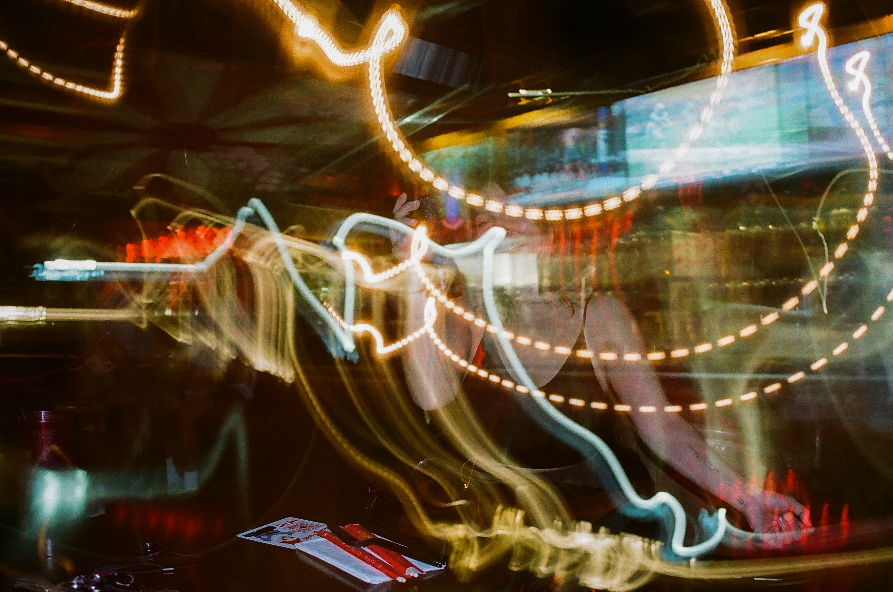 Friend poses for a picture during dinner at Shady Park in Tempe; camera's exposure settings creates motion blur of lights in the restaurant and blocks the view of her.