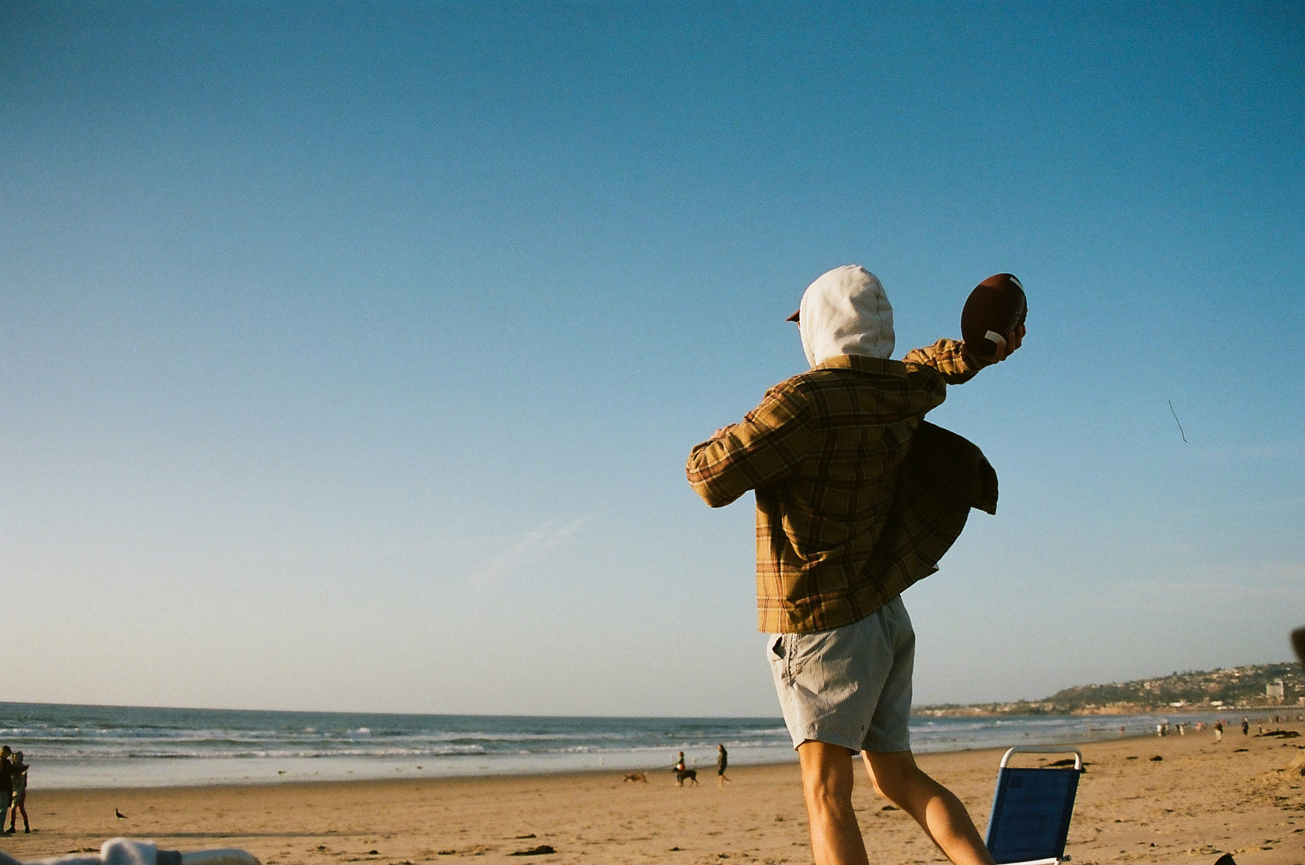 Friend throws football on the beach in San Diego.