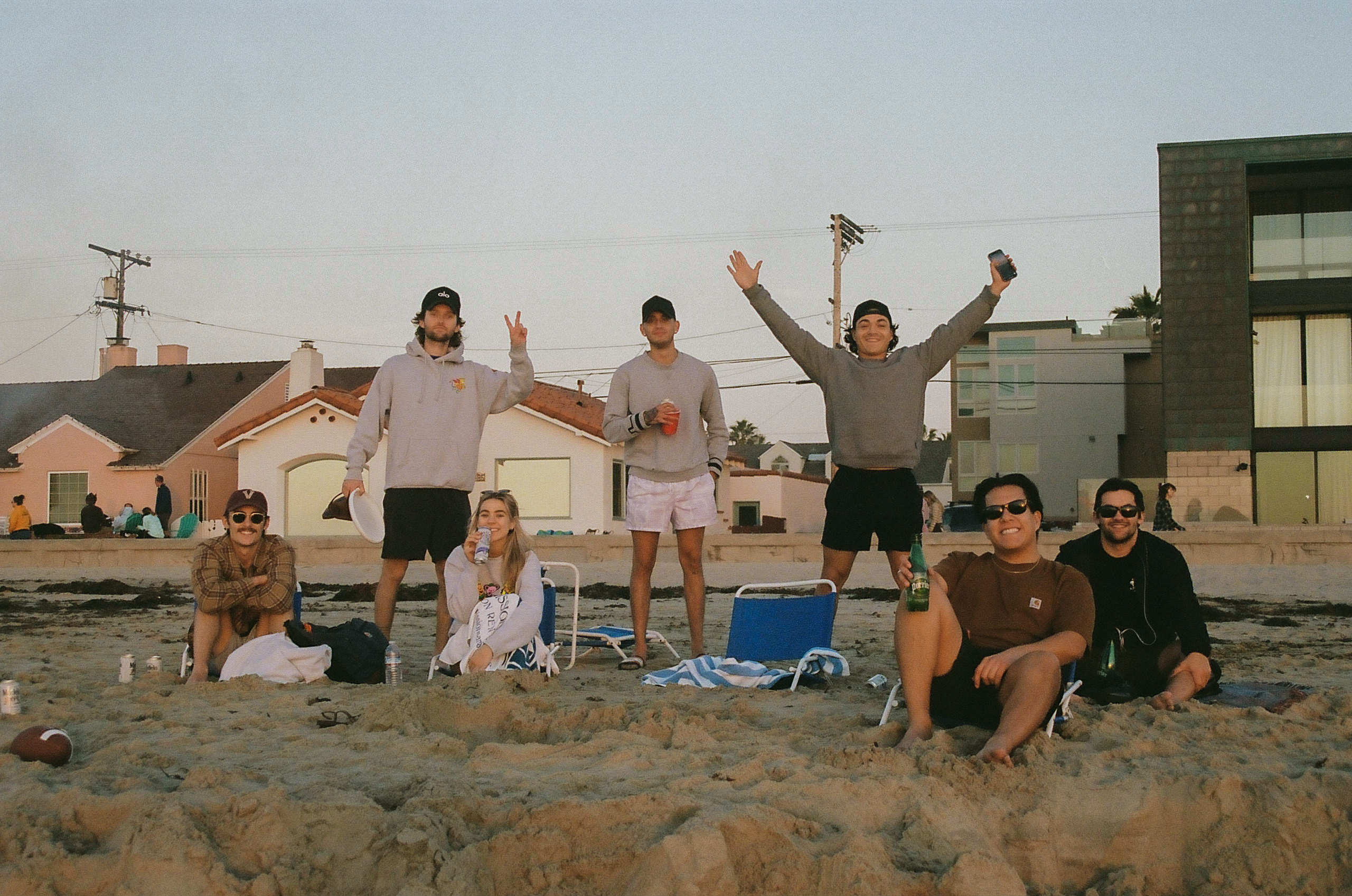 Group of friends smile for a picture while sitting on the beach in San Diego waiting to watch the first sunset of the new year.