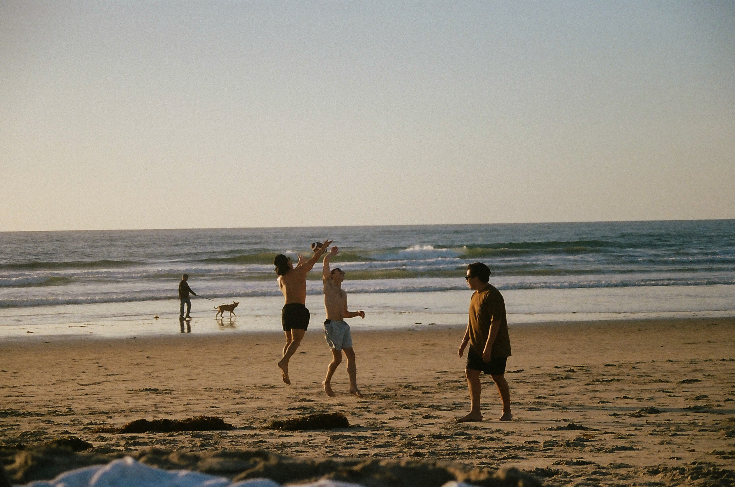 Two friends both jump up to catch a football while the third friend watches.