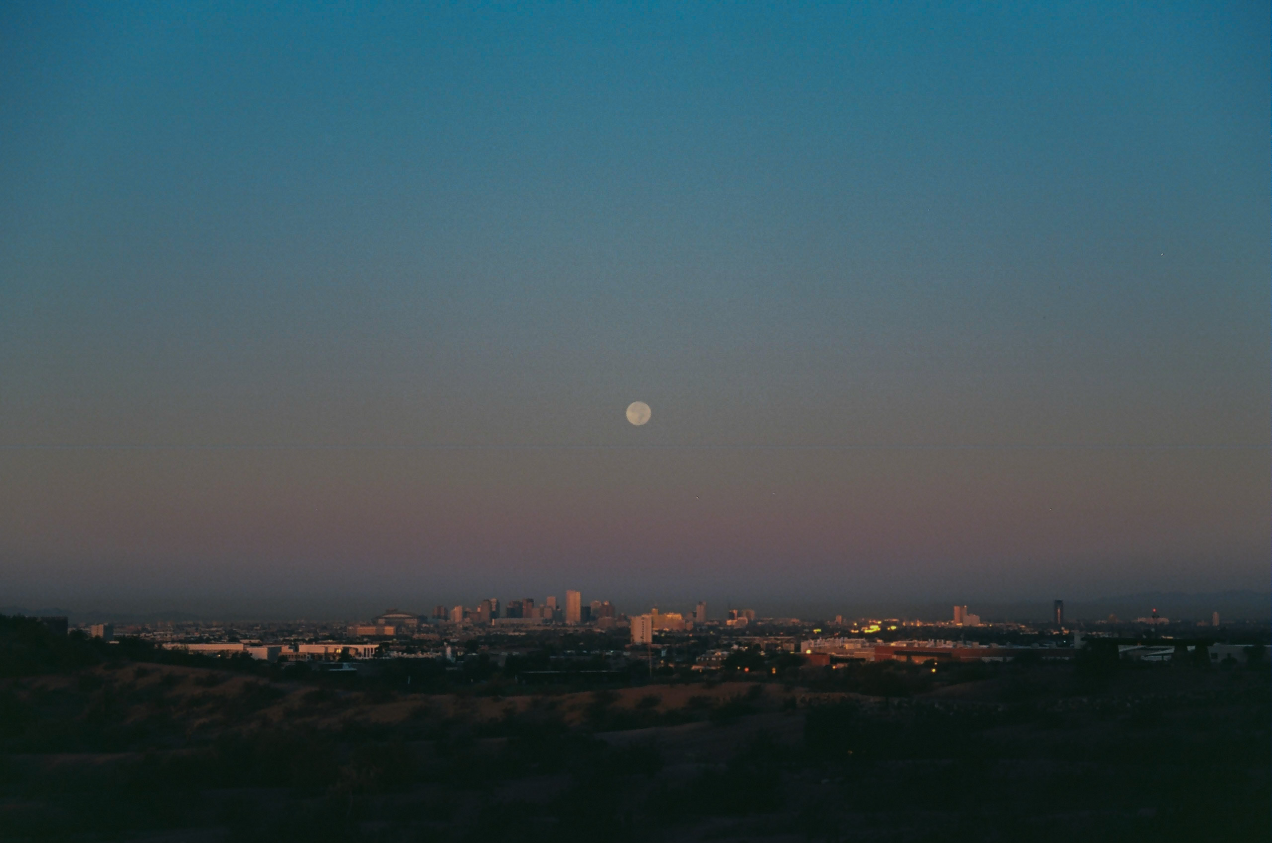 View from Papago Park of the moon resting above the city of Phoenix shortly after the sun sets.